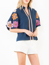 Load image into Gallery viewer, Navy textured top with bold floral embroidered sleeves and scalloped trim detail, paired with white shorts - 7
