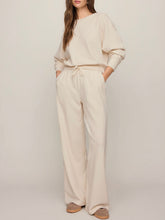 Load image into Gallery viewer, Woman wearing cream wide-leg drawstring lounge pants with matching sweatshirt and tan suede sneakers - 1
