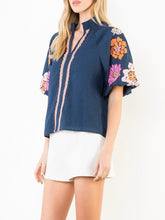 Load image into Gallery viewer, Navy textured top with bold floral embroidered sleeves and scalloped trim detail, paired with white shorts - 2
