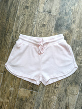 Load image into Gallery viewer, Light pink thermal waffle knit drawstring shorts with curved hem, laid flat on wood floor - 1
