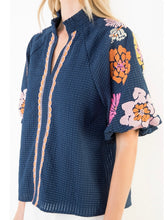 Load image into Gallery viewer, Navy textured top with bold floral embroidered sleeves and scalloped trim detail, paired with white shorts - 4
