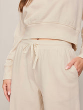 Load image into Gallery viewer, Woman wearing cream wide-leg drawstring lounge pants with matching sweatshirt and tan suede sneakers - 2
