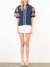 Load image into Gallery viewer, Navy textured top with bold floral embroidered sleeves and scalloped trim detail, paired with white shorts - 3
