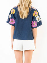 Load image into Gallery viewer, Navy textured top with bold floral embroidered sleeves and scalloped trim detail, paired with white shorts - 5
