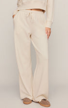 Load image into Gallery viewer, Woman wearing cream wide-leg drawstring lounge pants with matching sweatshirt and tan suede sneakers - 4

