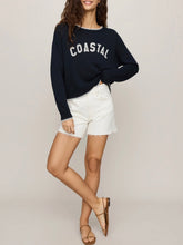 Load image into Gallery viewer, Woman wearing navy blue Coastal Sienna Sweater in Eclipse with white letter graphic and cream denim shorts - 3
